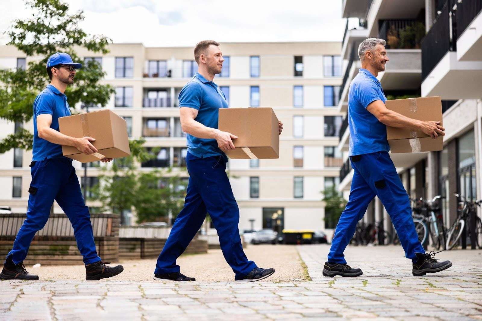 three Dighton MA movers dressed in blue walking in a line, each carrying a box.