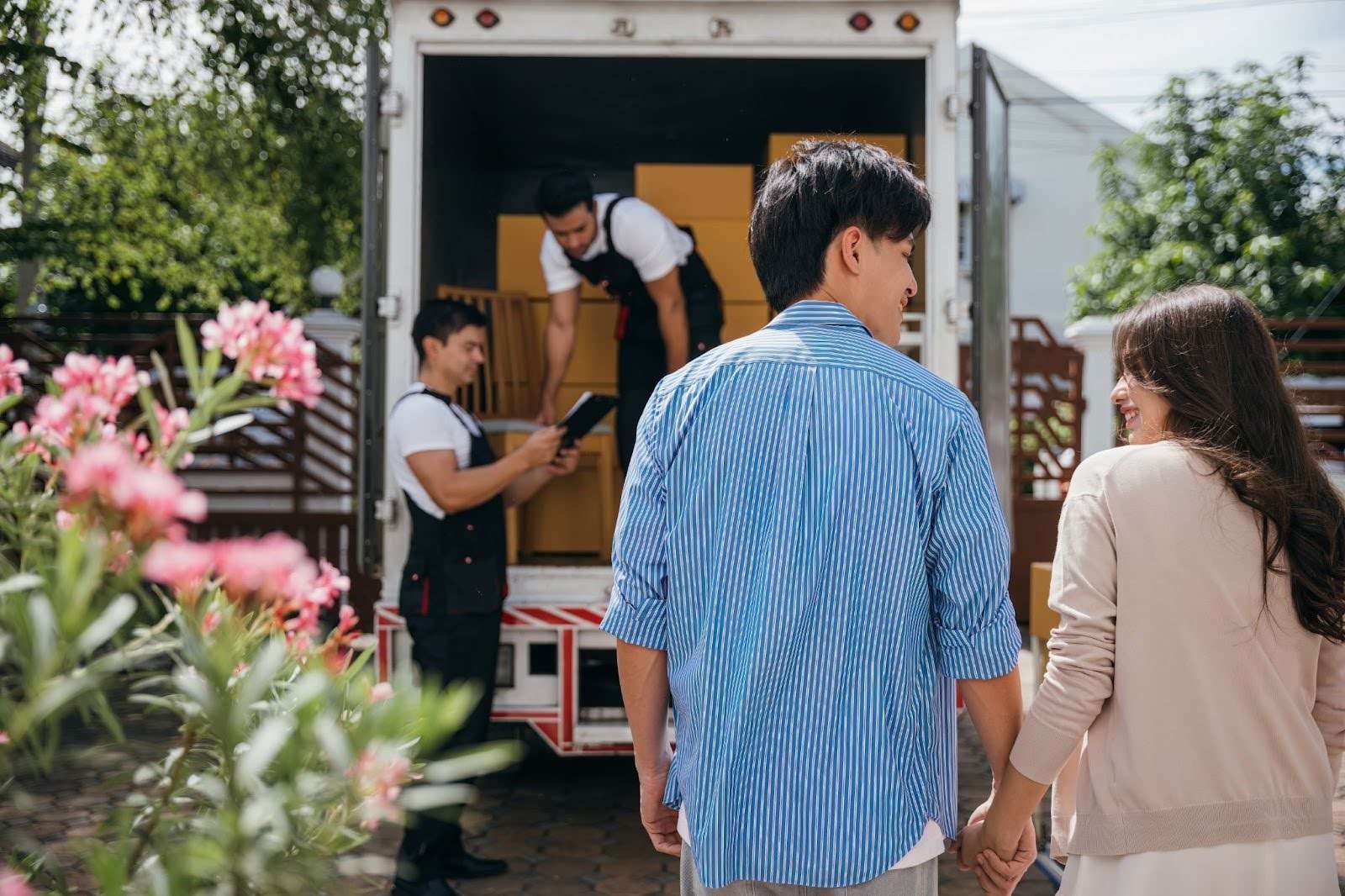 Young couple holding hands and watching Dighton MA movers load their belongings into a moving truck
