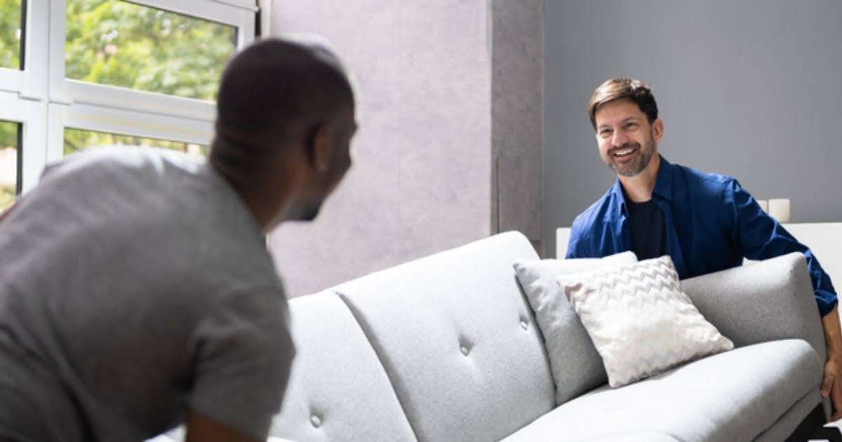 Two movers in Holden MA handling a white sofa in a living room