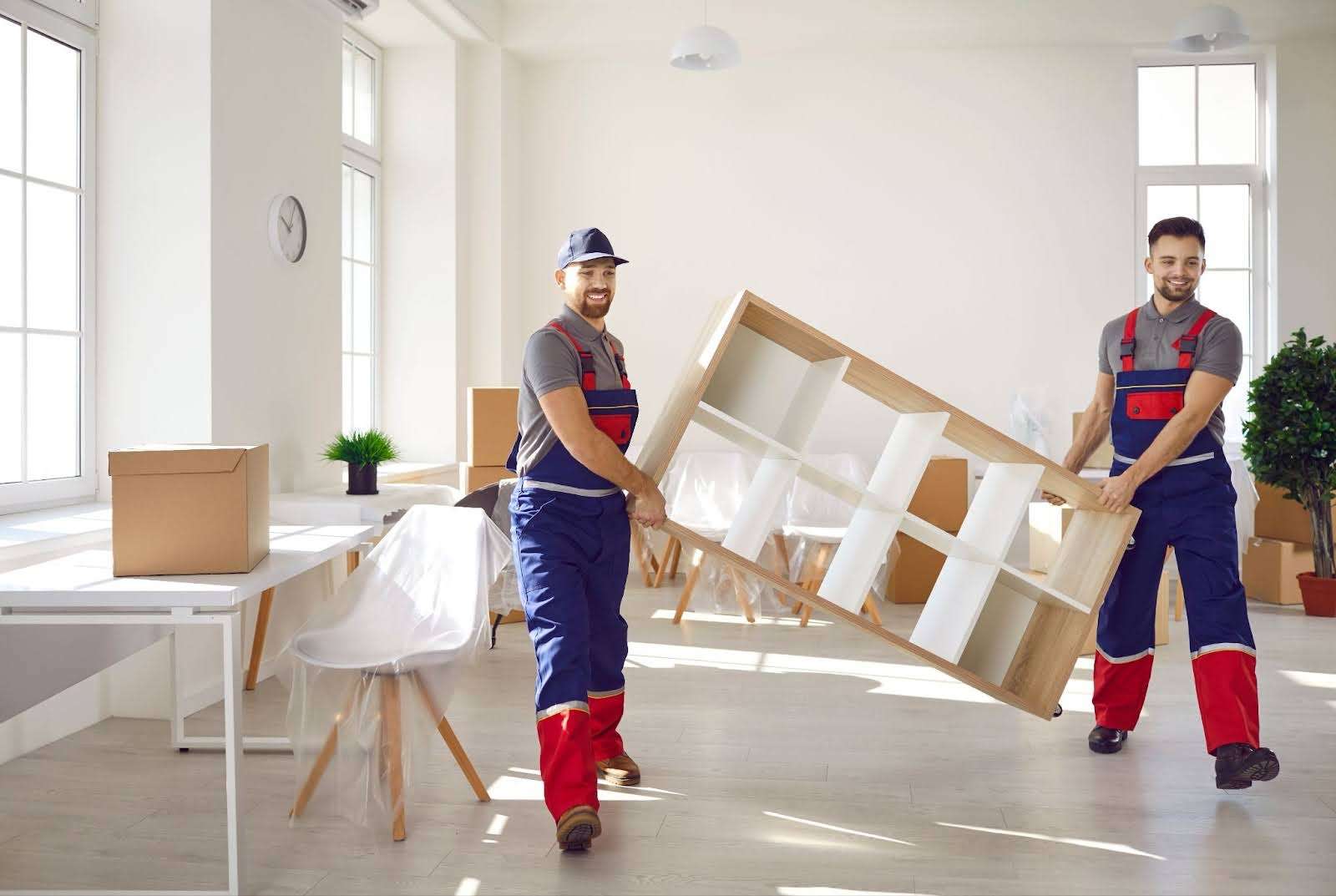 Two Gardner MA movers in overalls smiling and carrying a shelf out of a home