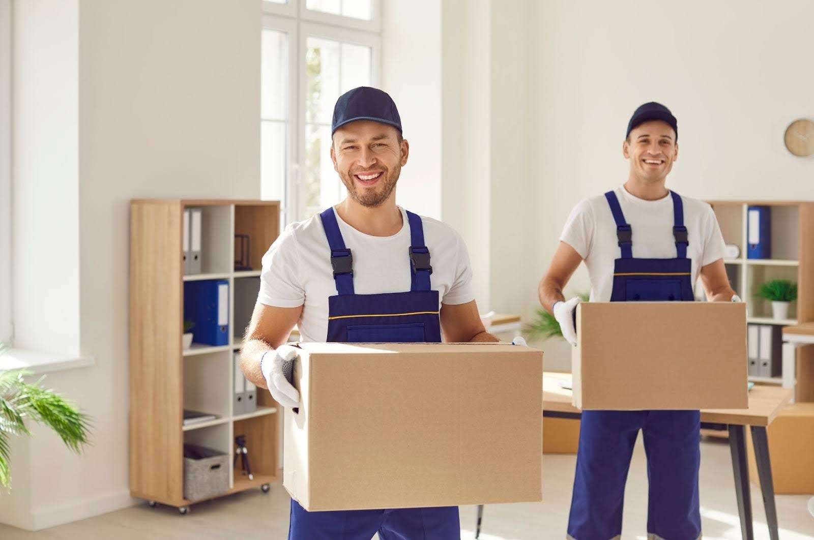 two Dudley MA movers in blue overalls holding boxes and smiling