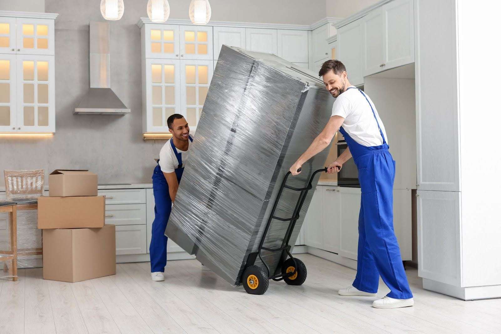 two Dudley MA movers wheeling a plastic-wrapped refrigerator into a kitchen